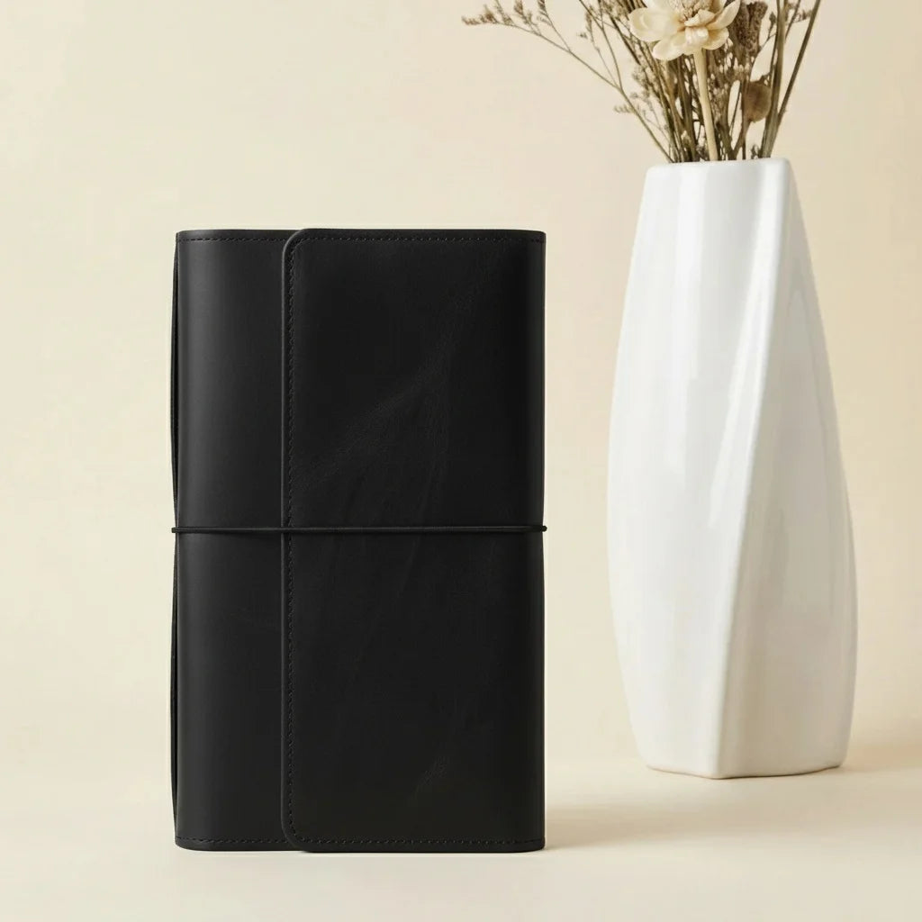 Brown leather notebook next to a white vase with dried flowers on a beige background