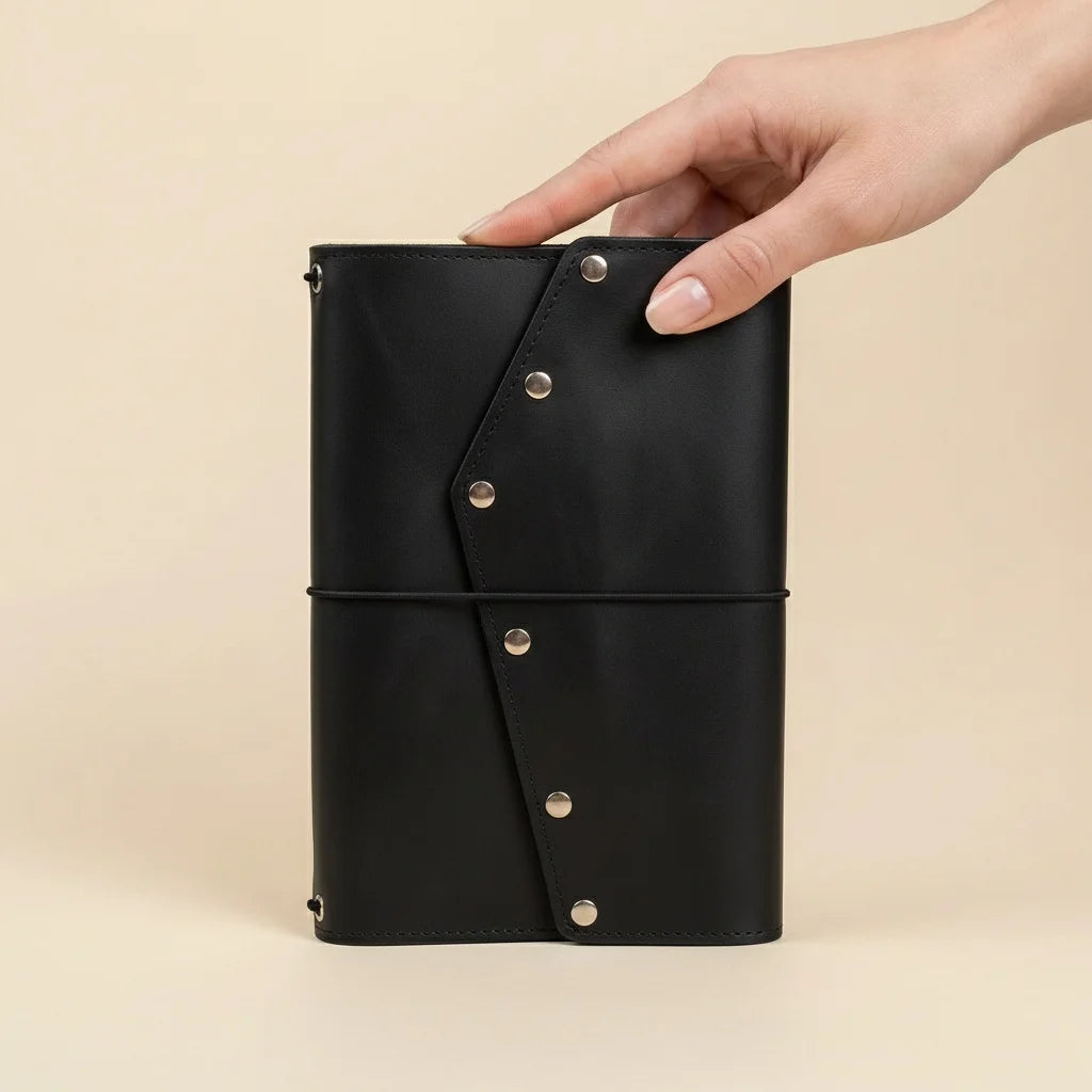 Black leather notebook with button details held by a hand on a beige background