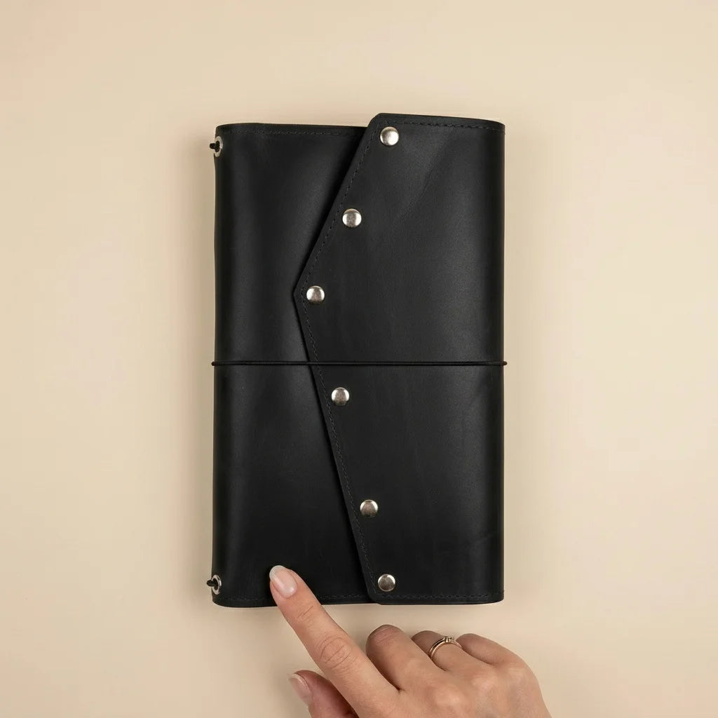 Black leather journal with silver buttons held by a hand on a beige background
