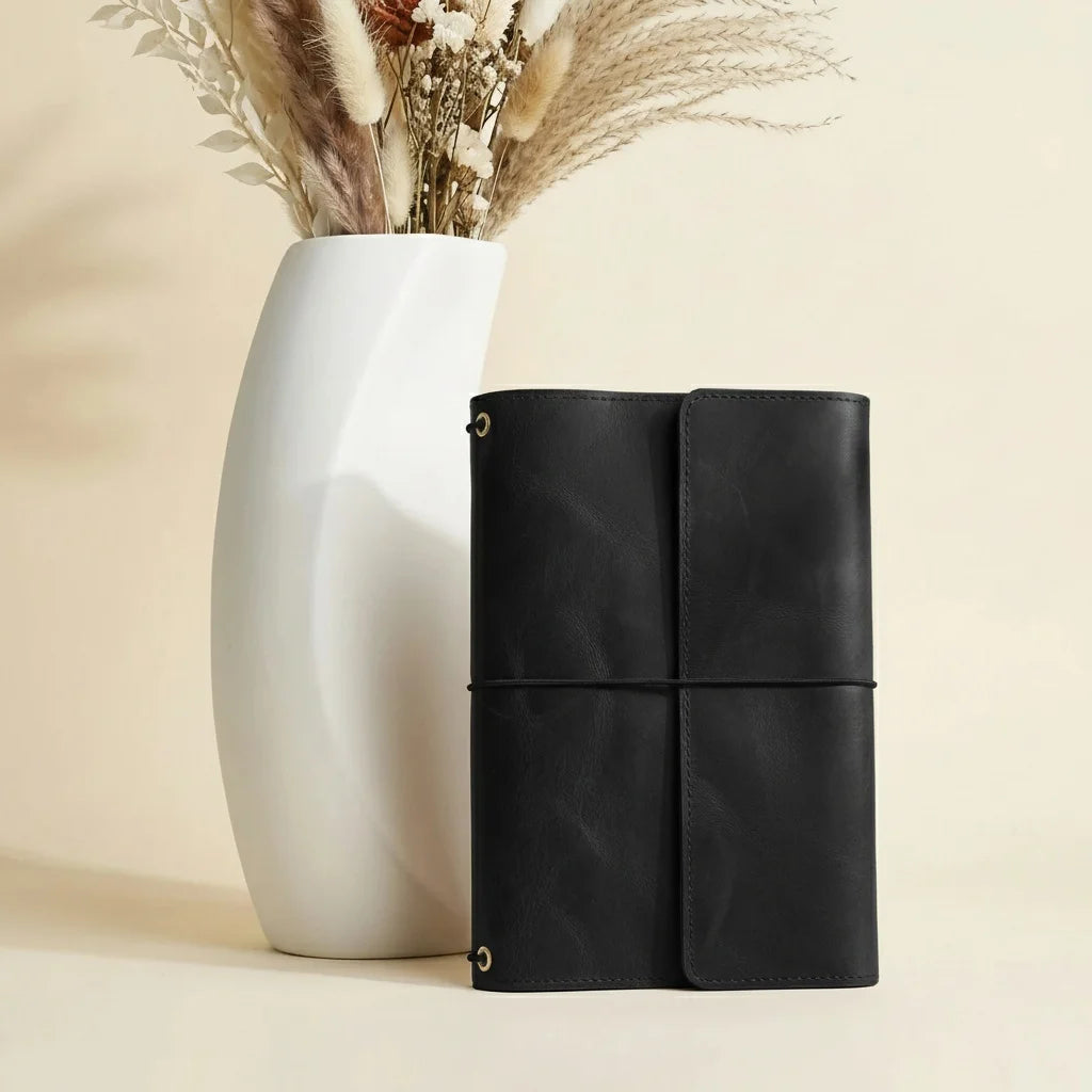 Black leather notebook with a white vase and dried plants on a beige background
