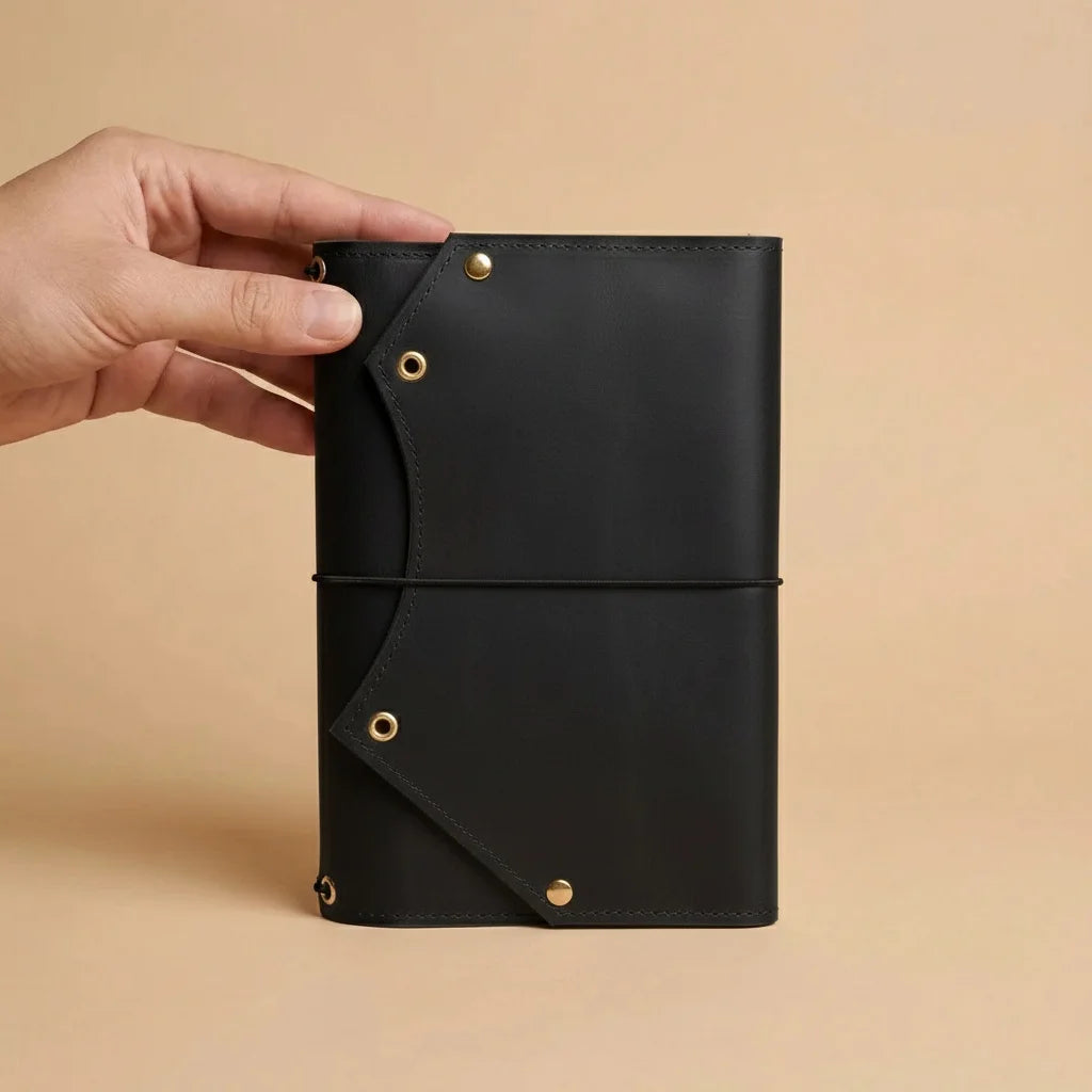 Hand holding a black leather notebook with gold accents on a beige background