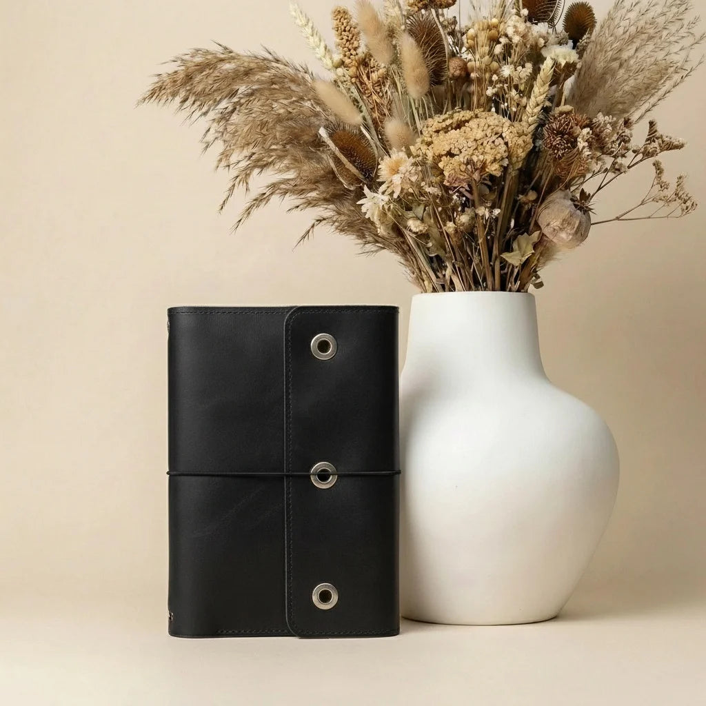 Green leather notebook and white vase with dried flowers on a beige background