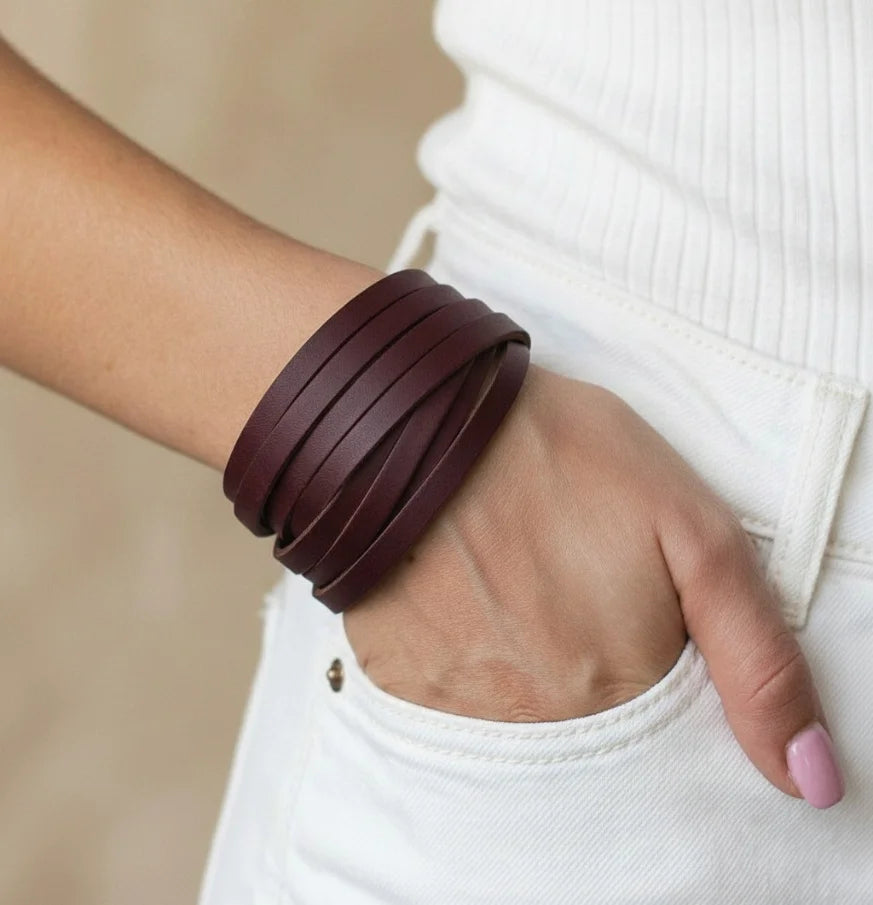 Person wearing multiple brown leather bracelets on a neutral background