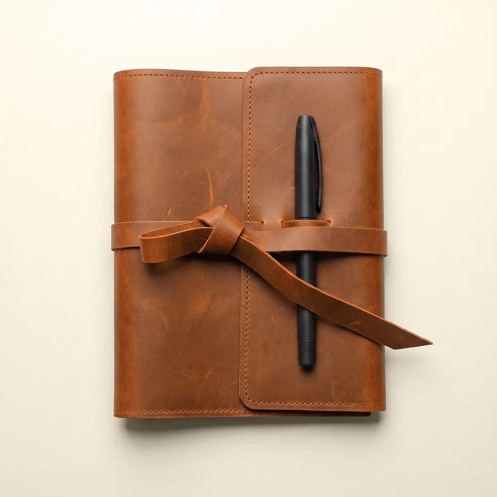 Handmade leather notebook with storage pockets and integrated leather pen loop.