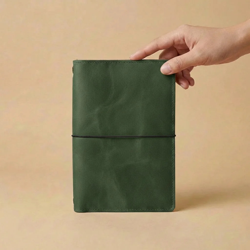 Hand holding a green notebook against a beige background
