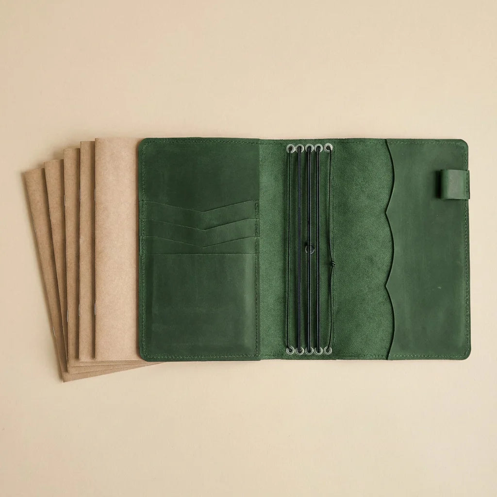 Green leather journal cover held open by a hand on a beige background