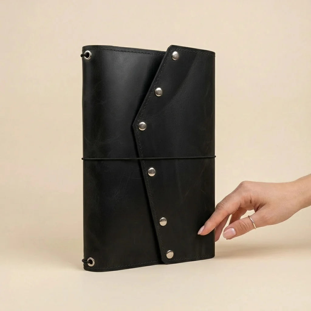 Black leather clutch with silver buttons held by a hand on a beige background
