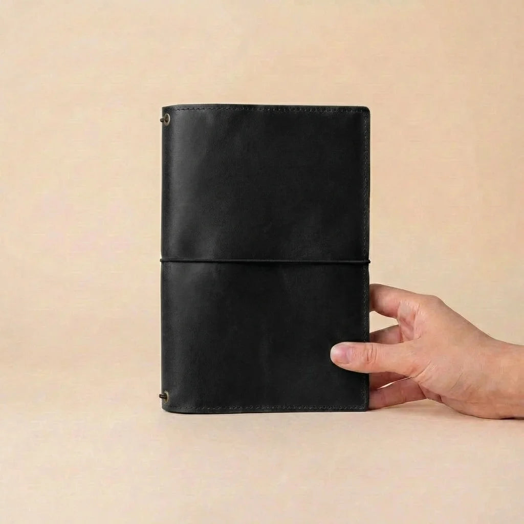 Black leather notebook held by a hand against a beige background