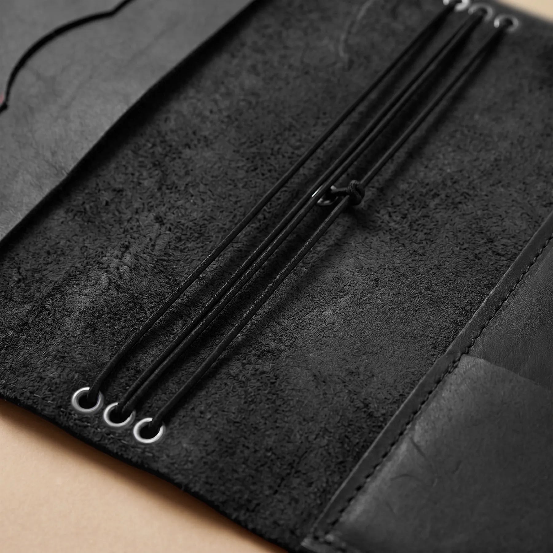 Close-up of a black textured journal with metal accents on a beige surface