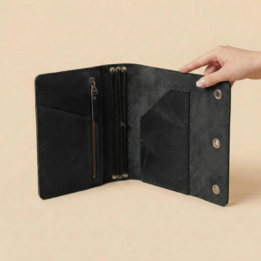 Black leather journal with gold accents held open by a hand on a beige background