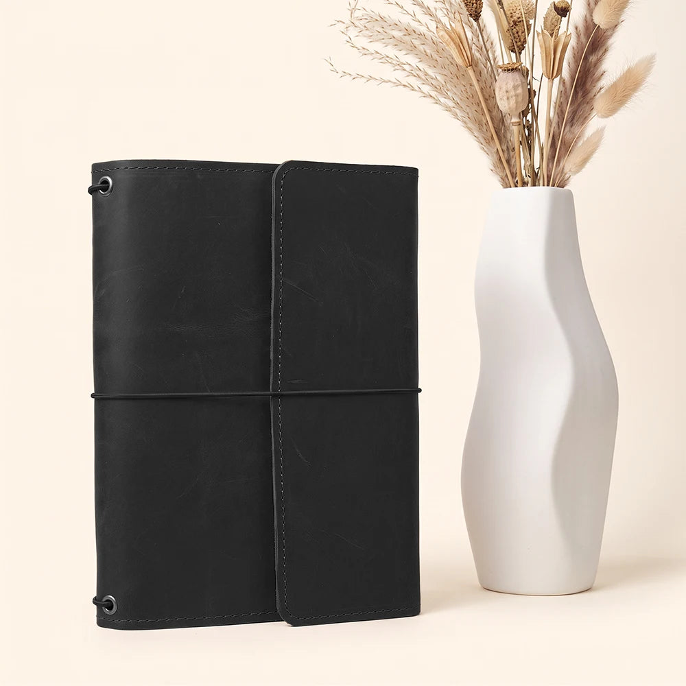 Handmade leather notebook cover with secure refillable design and organized accessory storage inside.