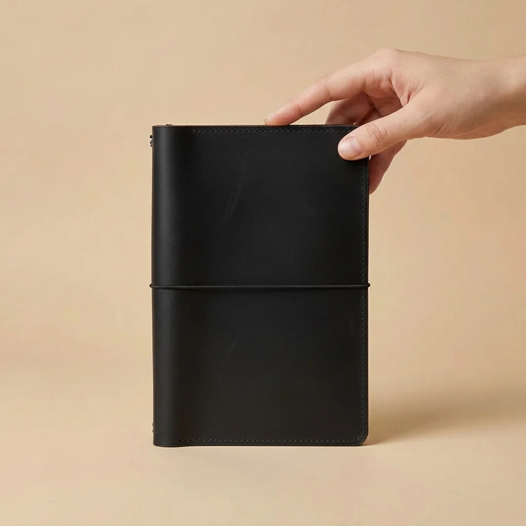 Black leather notebook held by a hand against a beige background