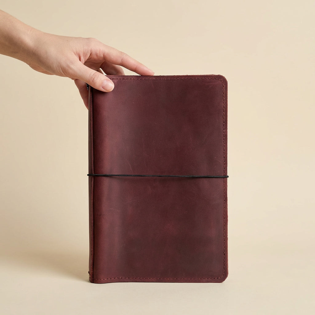 Brown leather notebook held by a hand on a beige background