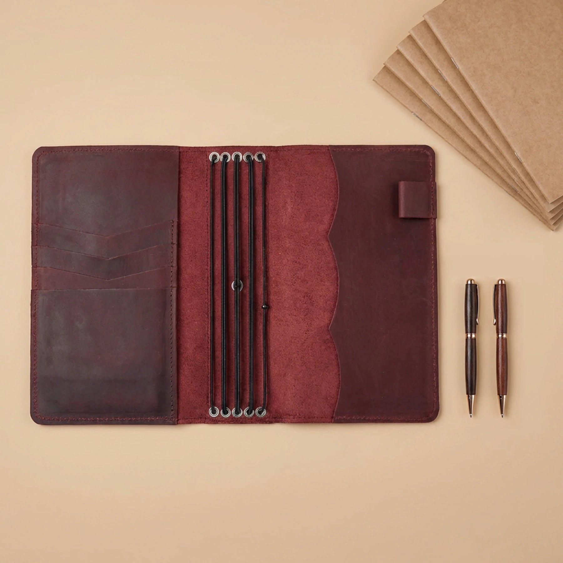 Brown leather notebook with pen holder and pens on a beige background