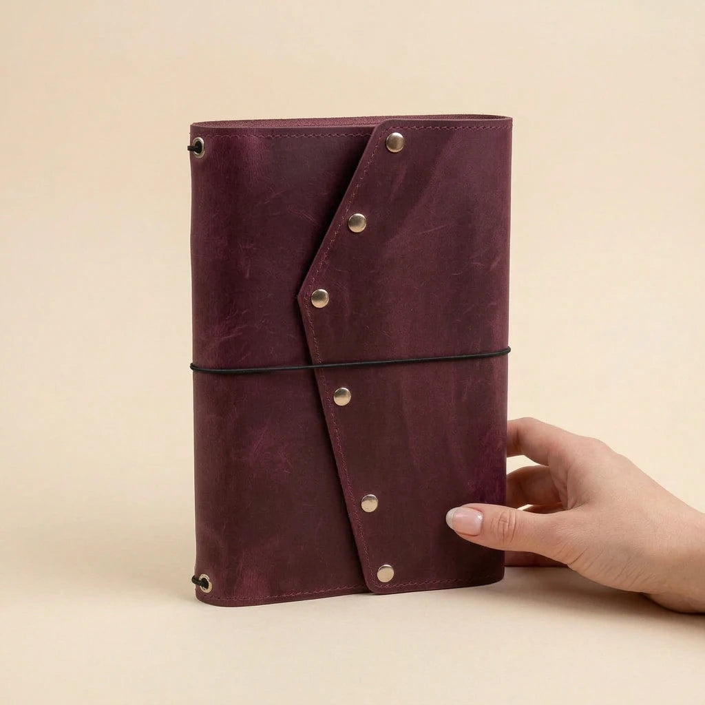 Hand holding a maroon leather-bound notebook against a beige background
