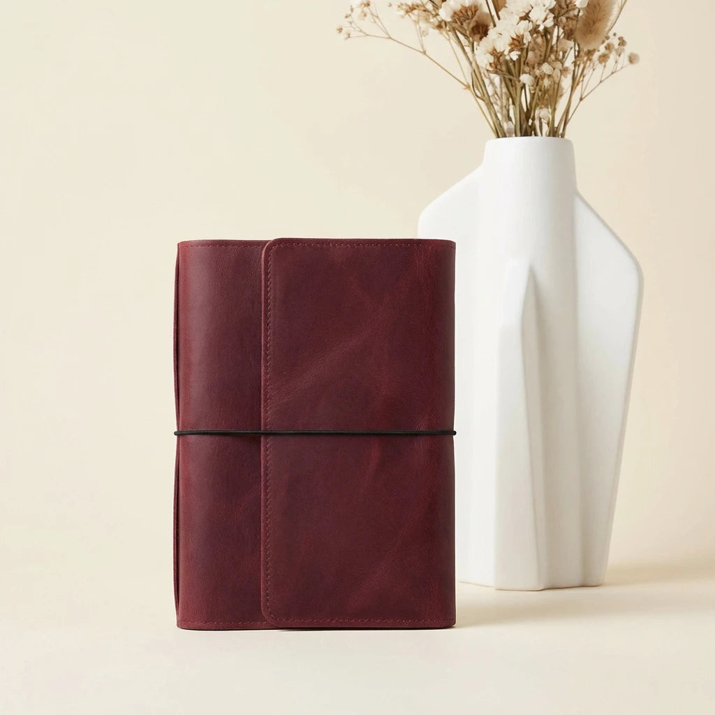 Brown leather notebook next to a white vase with dried flowers on a beige background