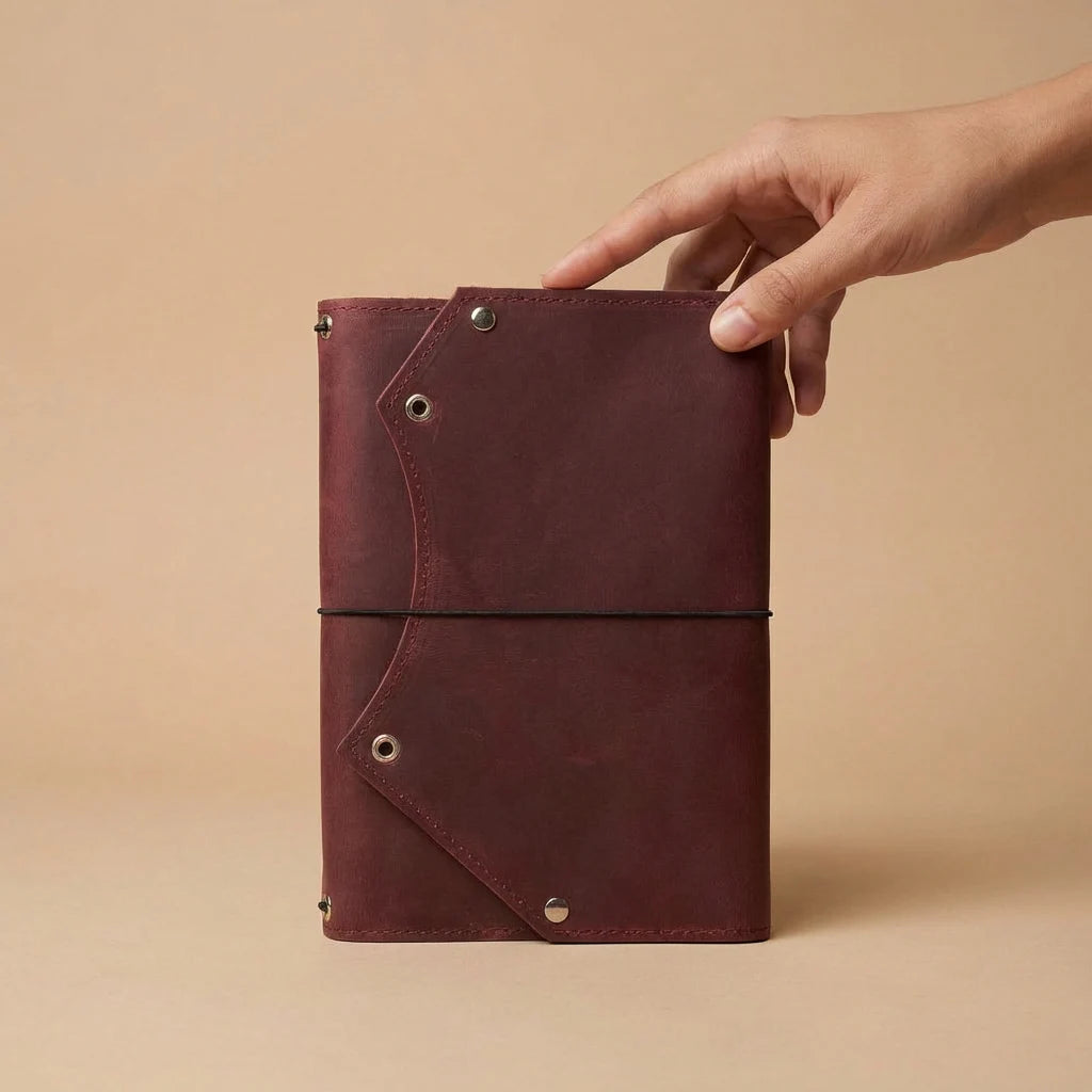 Hand holding a maroon leather notebook against a beige background