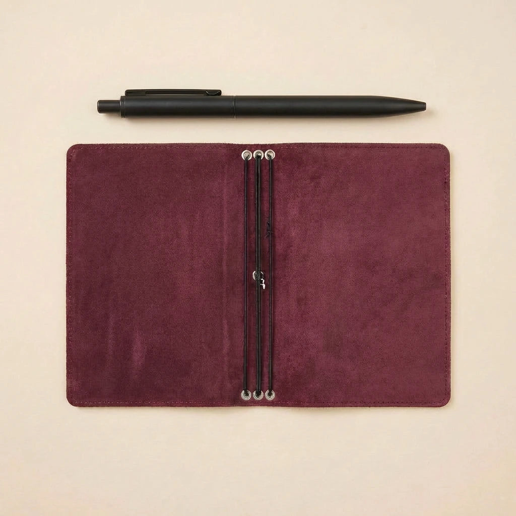 Maroon leather notebook with pen on a beige background