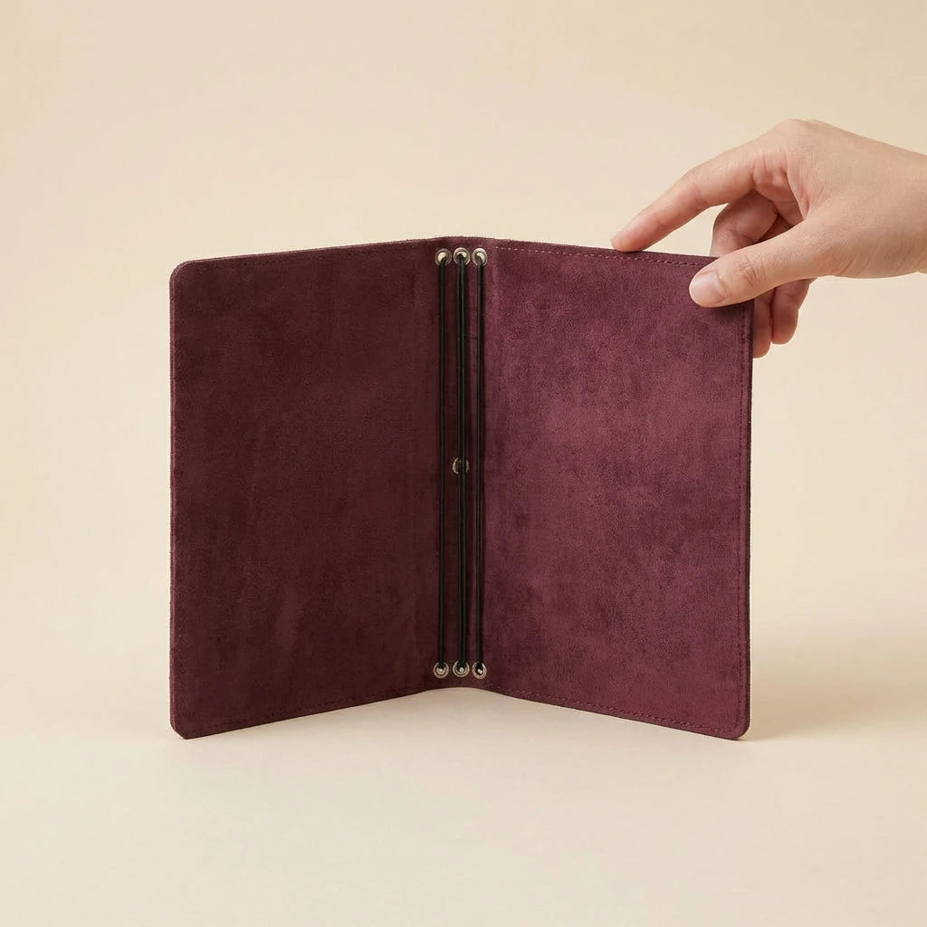 Hand holding a burgundy leather journal cover against a beige background