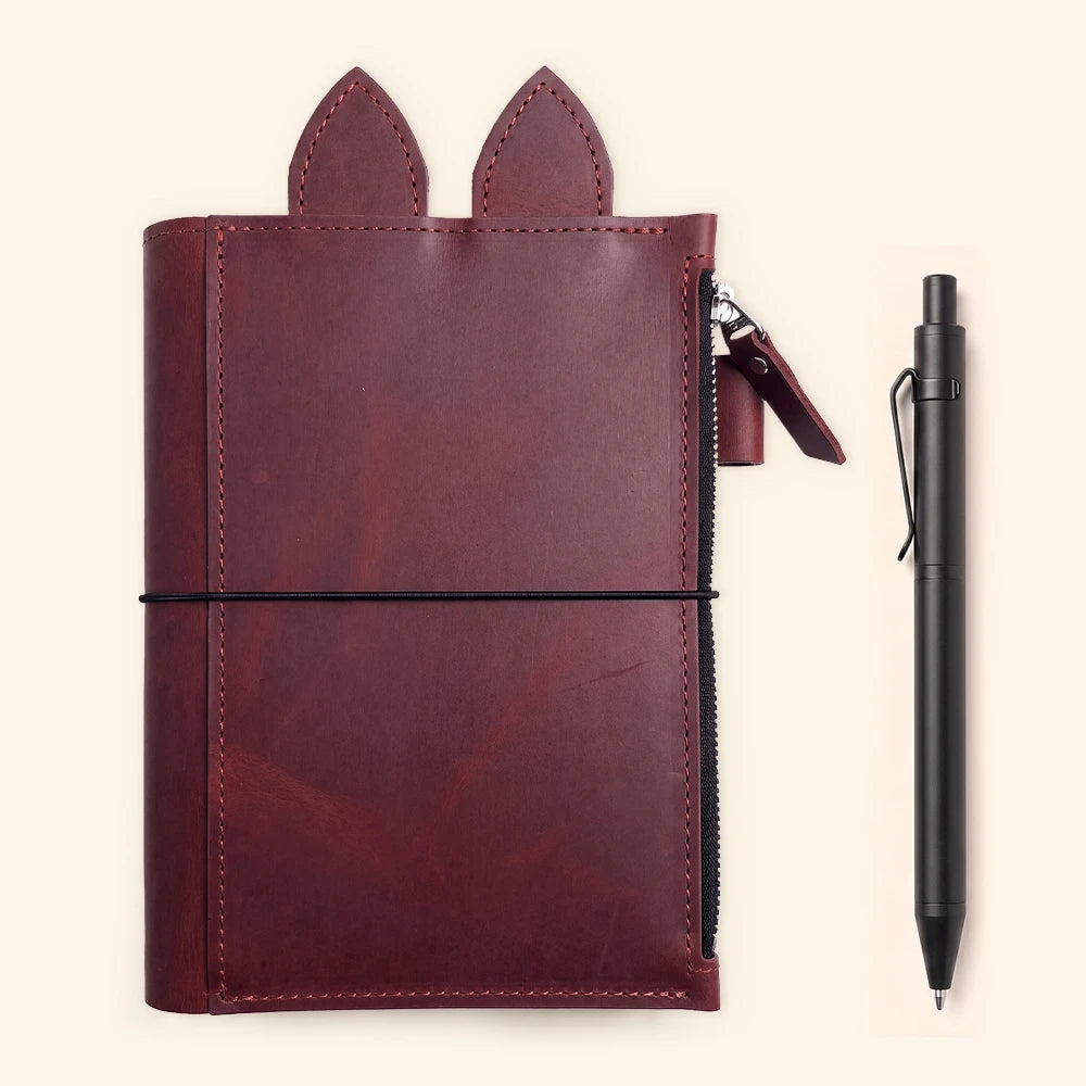 Leather planner cover opened flat with decorative ear tabs above the main pocket.