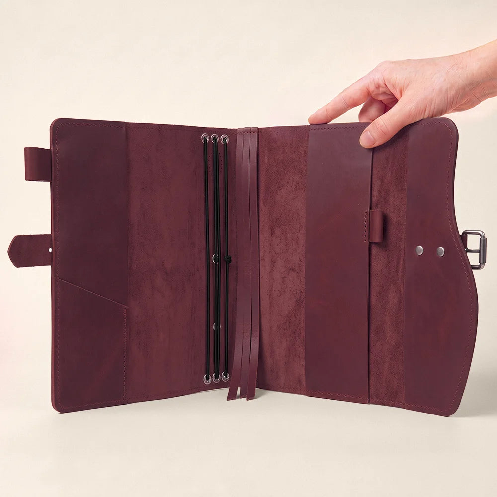 Handmade leather notebook organizer with interior storage, pen loop, attached marker, and convenient outer handle.