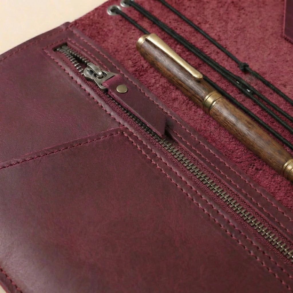 Close-up of a maroon leather pouch with a zipper, containing a wooden pen and black thread.