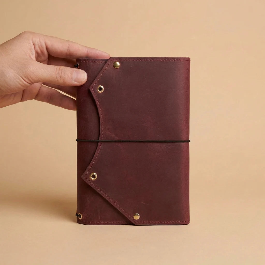 Brown leather notebook held by a hand against a beige background