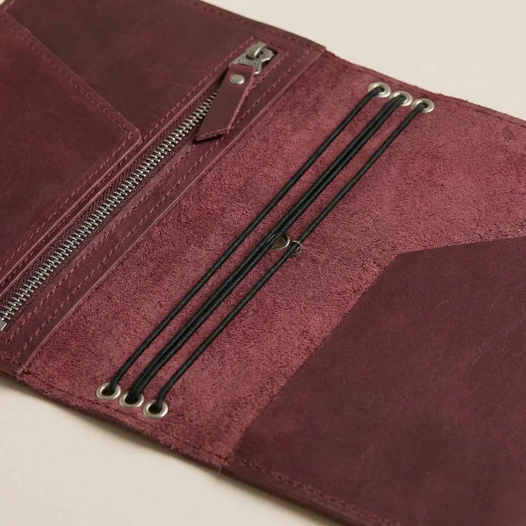 Close-up of a maroon leather journal with zipper and laces on a beige background