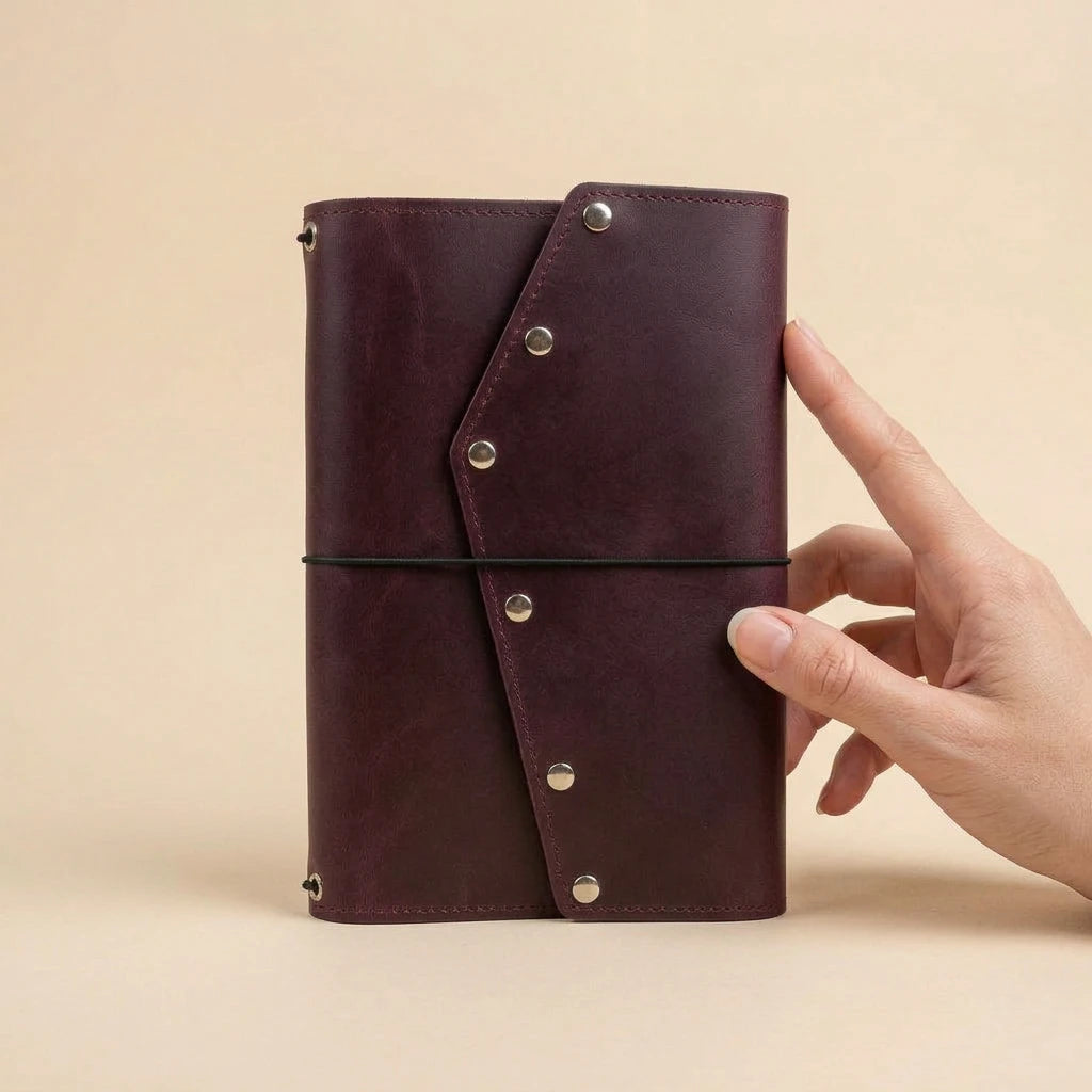 Hand holding a brown leather notebook with metal clasps on a beige background