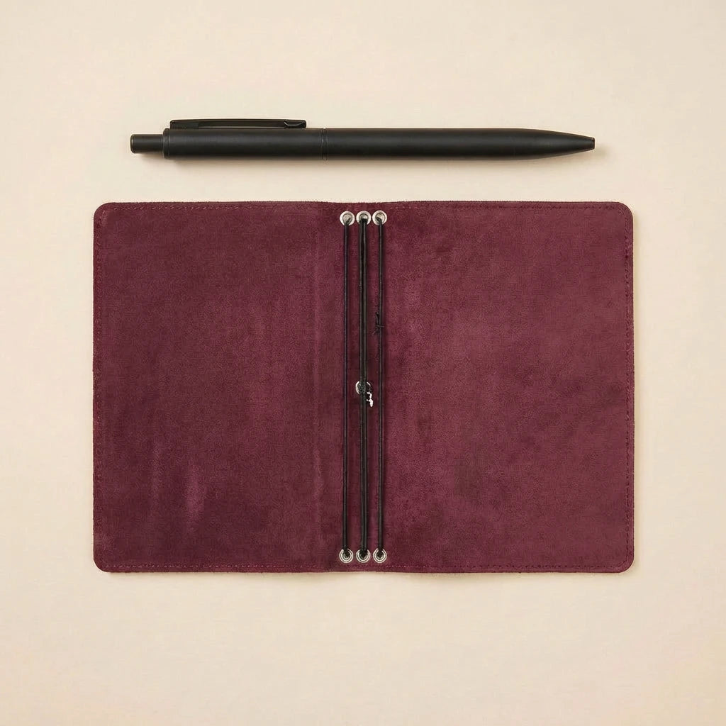 Maroon leather notebook with pen on a beige background
