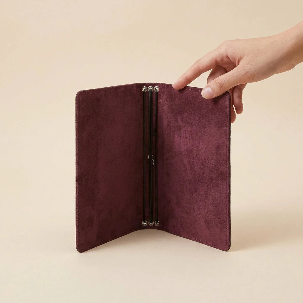 Hand holding a burgundy leather journal cover against a beige background