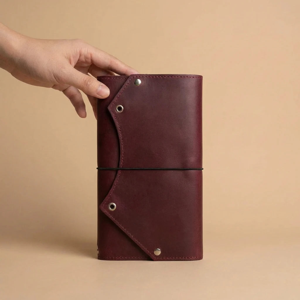 Brown leather notebook held by a hand against a beige background