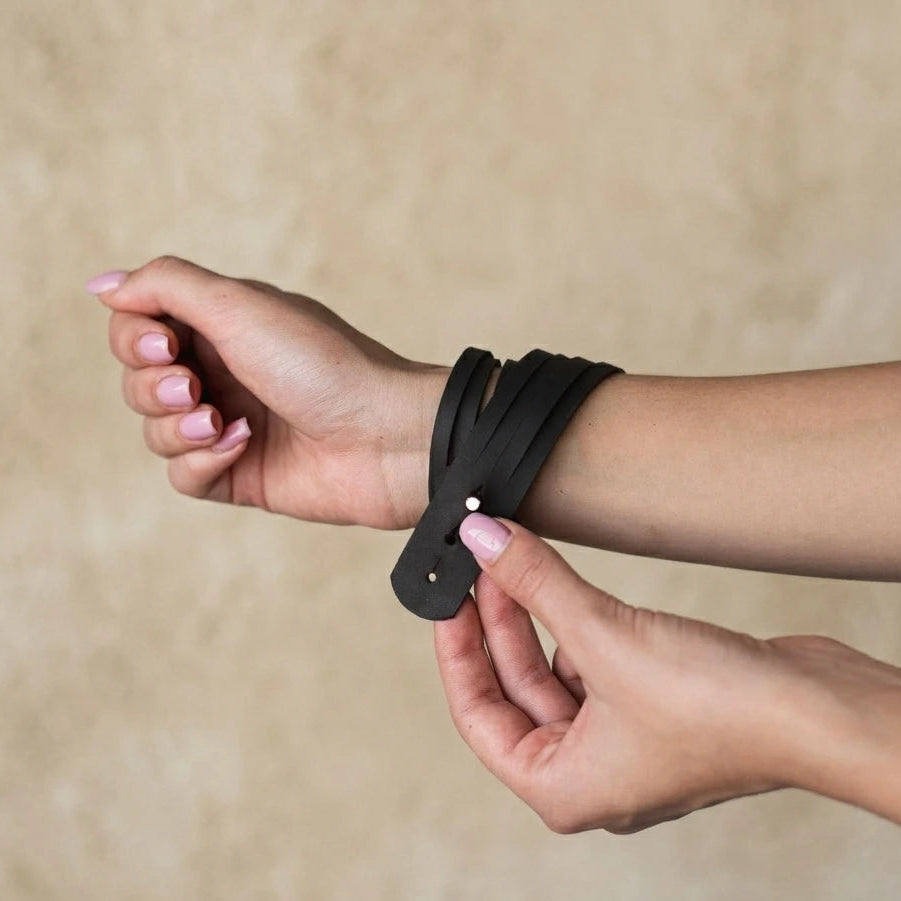 Person wearing a black leather bracelet on a beige background