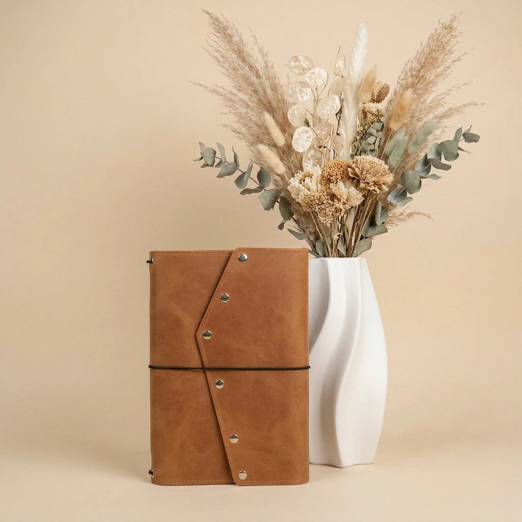Brown leather notebook with a white vase containing dried flowers on a beige background