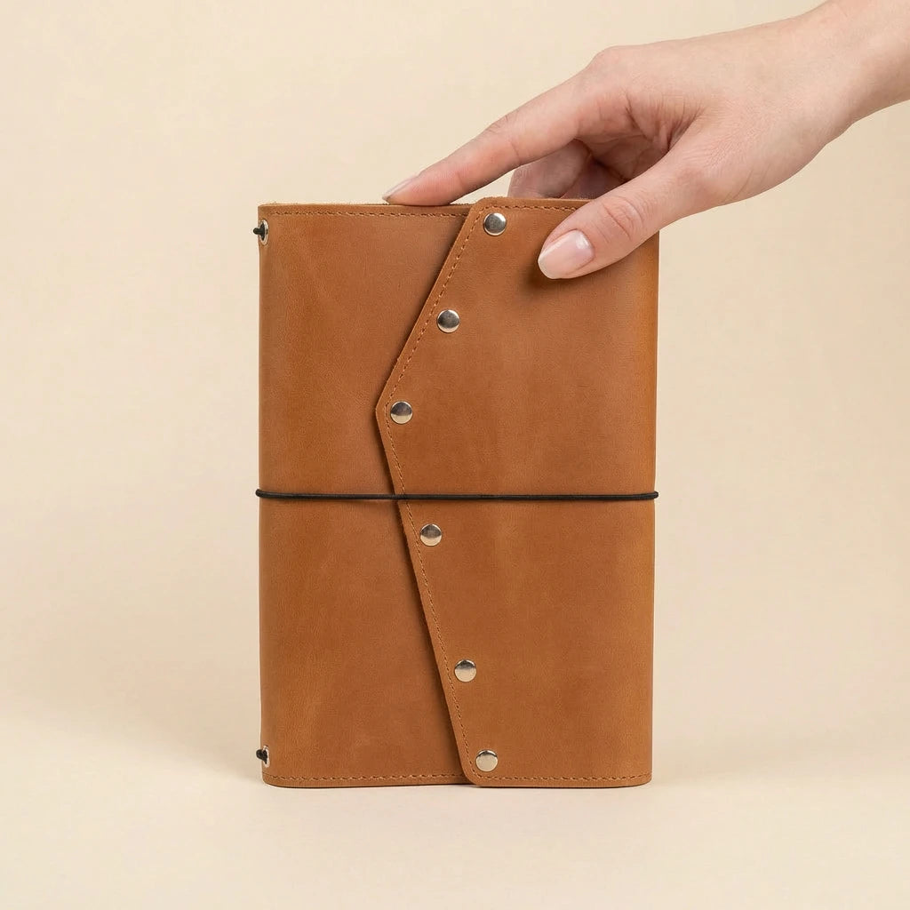 Brown leather notebook held by a hand on a beige background