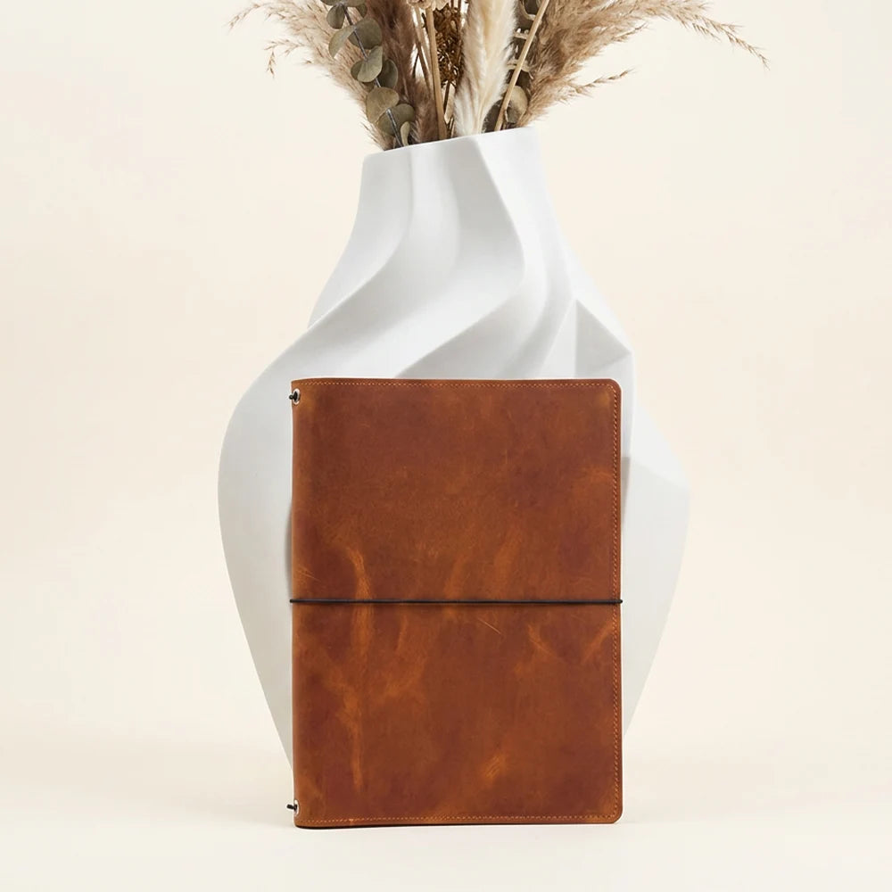 Leather journal cover opened to display pockets, elastic cords, and sketchbook fastening.