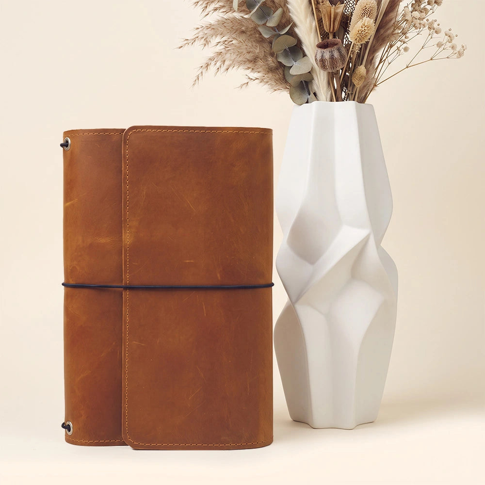 Refillable leather notebook case with structured storage layout and stitched pen carrying loop.