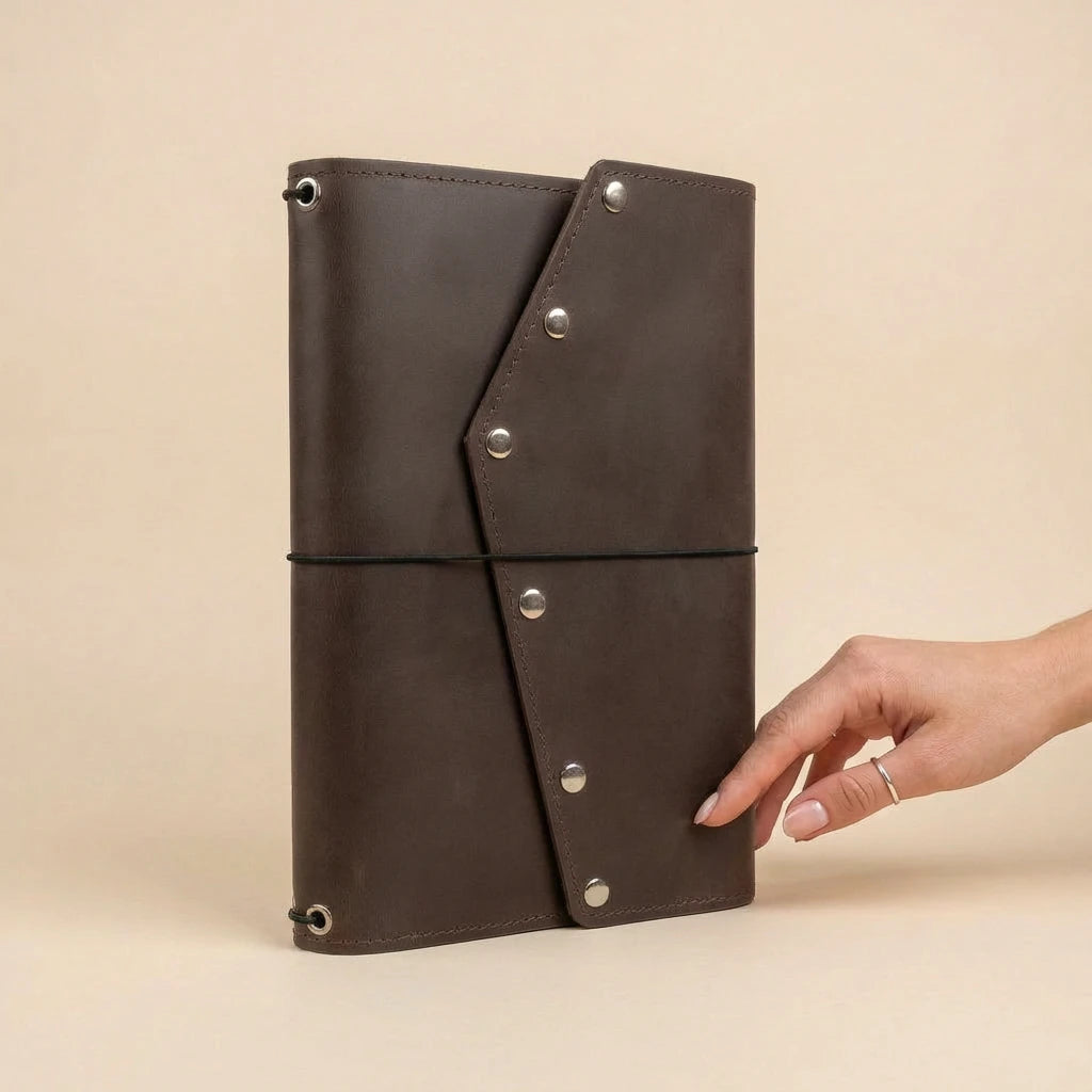 Brown leather journal with silver rivets held by a hand on a beige background