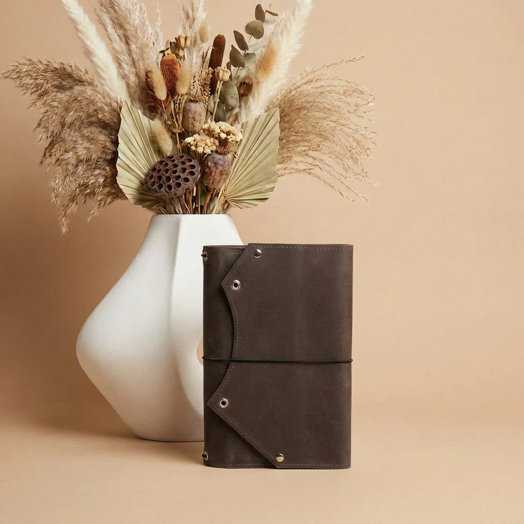 Brown leather notebook with decorative dried plants in a white vase on a beige background