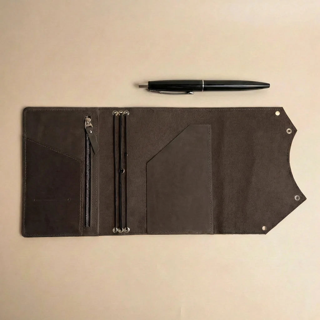 Black leather journal cover with zipper pocket and pen on a beige background
