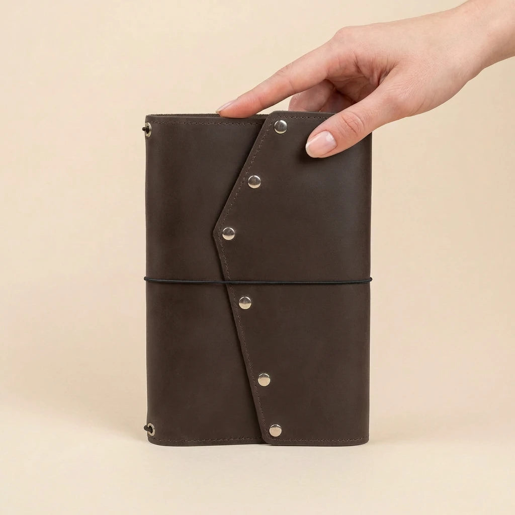 Brown leather notebook with metal rivets held by a hand on a beige background