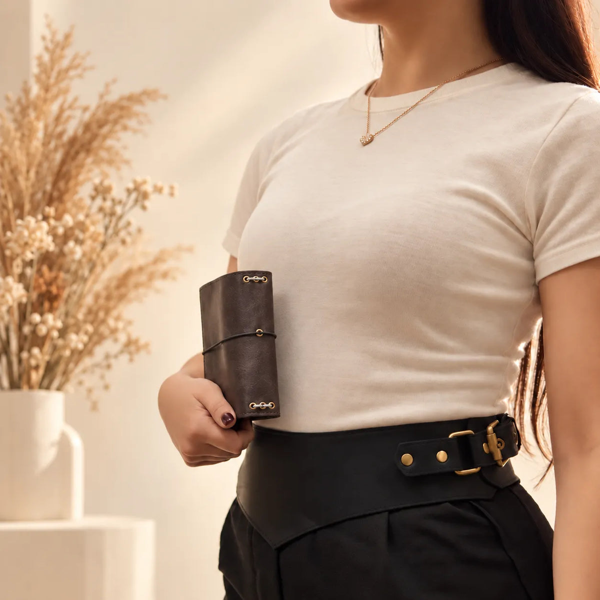 Young woman holding a handmade natural leather journal cover against a neutral background.
