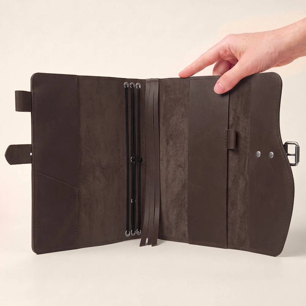 Natural hide notebook case displaying interior storage sections, pen loop, permanent bookmark, and exterior grab handle.