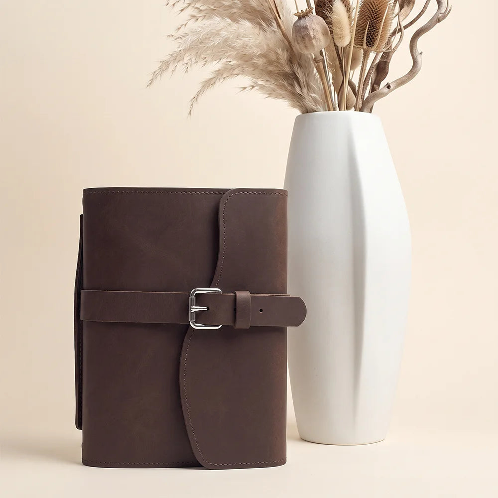 Handmade leather notebook carrier featuring inner pockets, elastic pen loop, integrated ribbon marker, and sturdy handle.