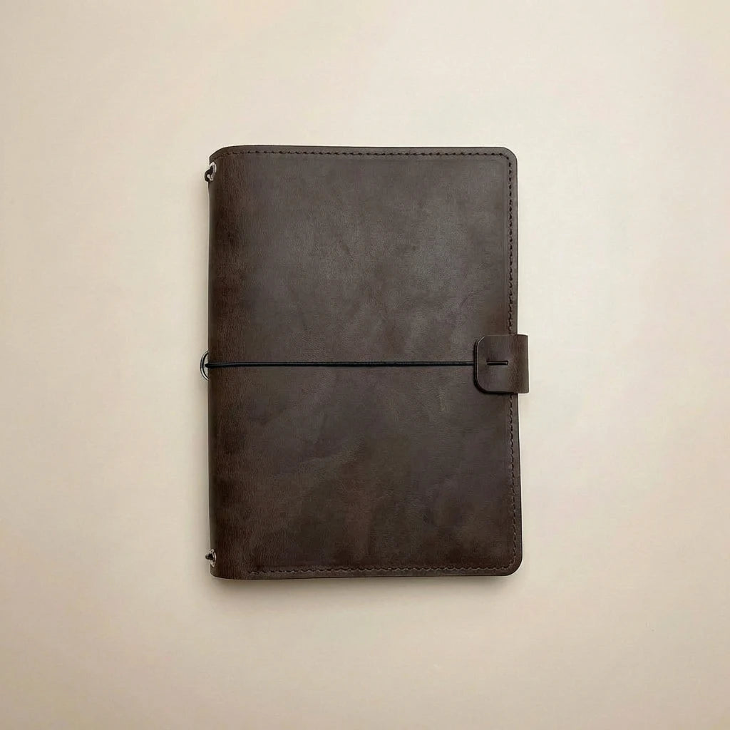 Dark brown leather notebook with a black strap on a beige background