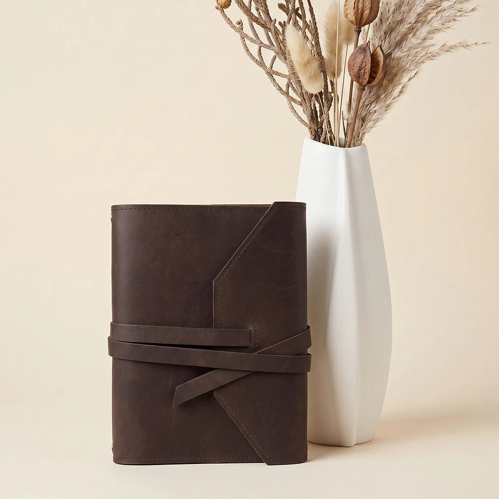 Refillable journal protector crafted from leather with elastics and pen loop.