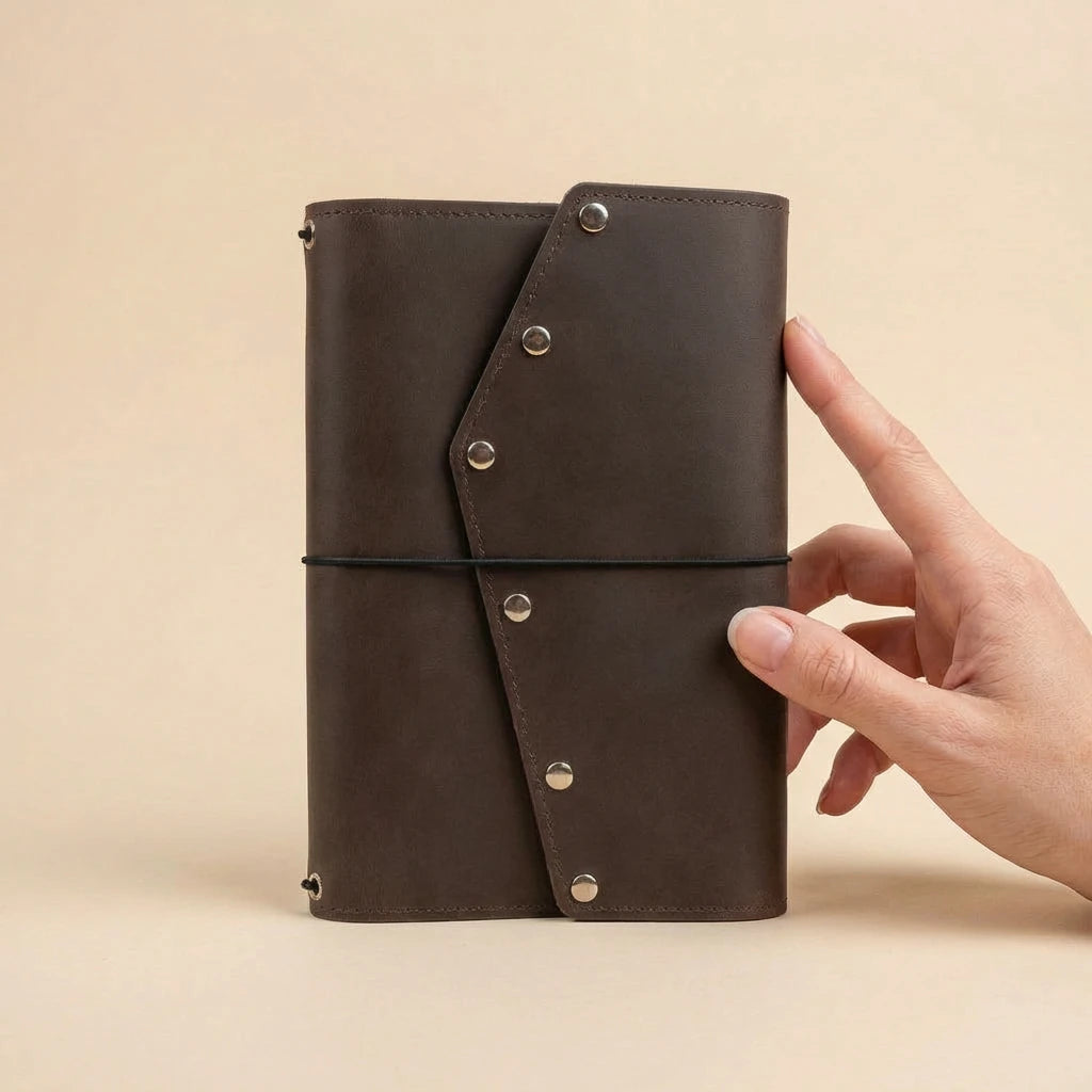 Brown leather journal held by a hand on a beige background