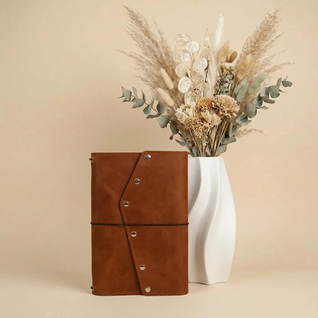 Brown leather notebook with a white vase containing dried flowers on a beige background