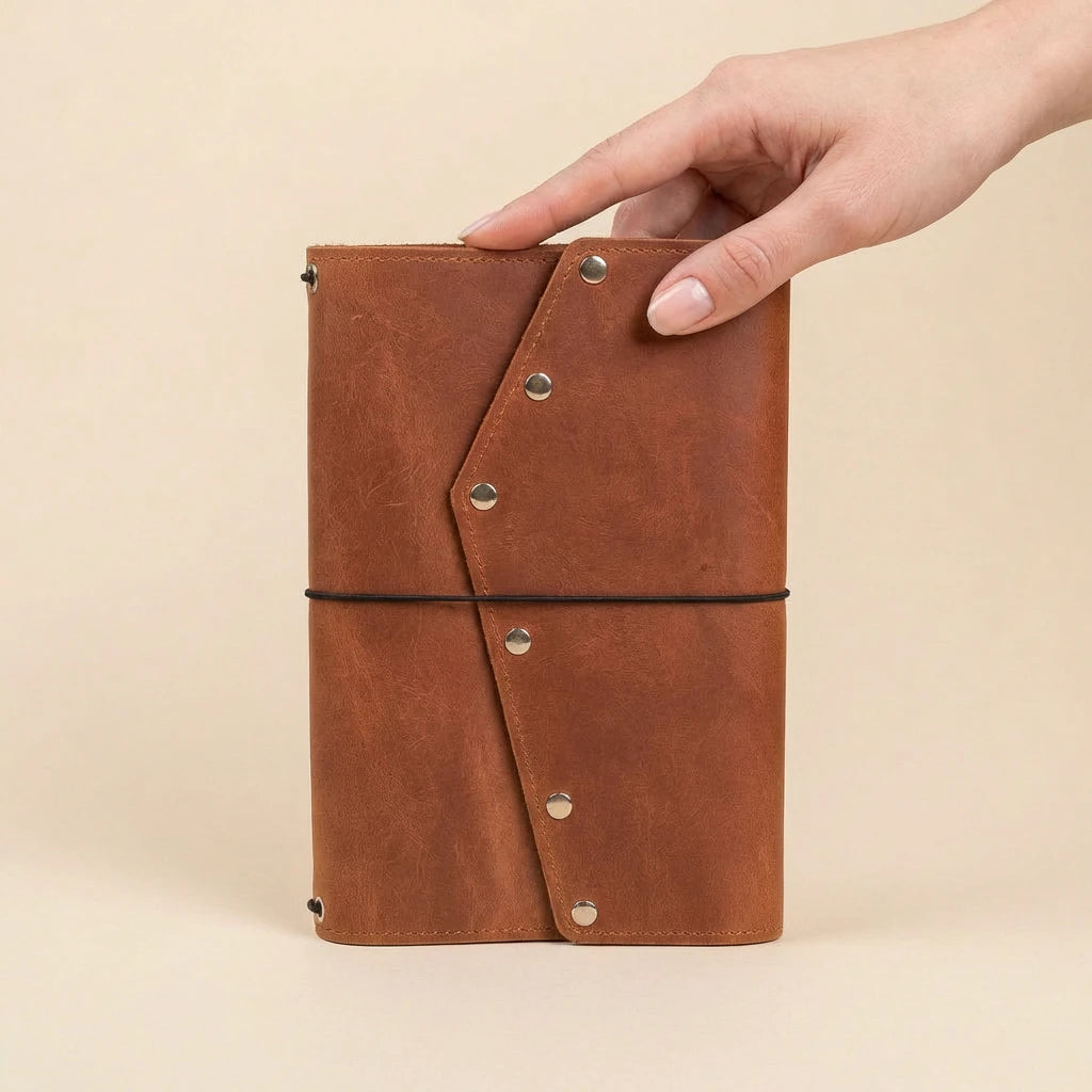 Brown leather notebook held by a hand on a beige background