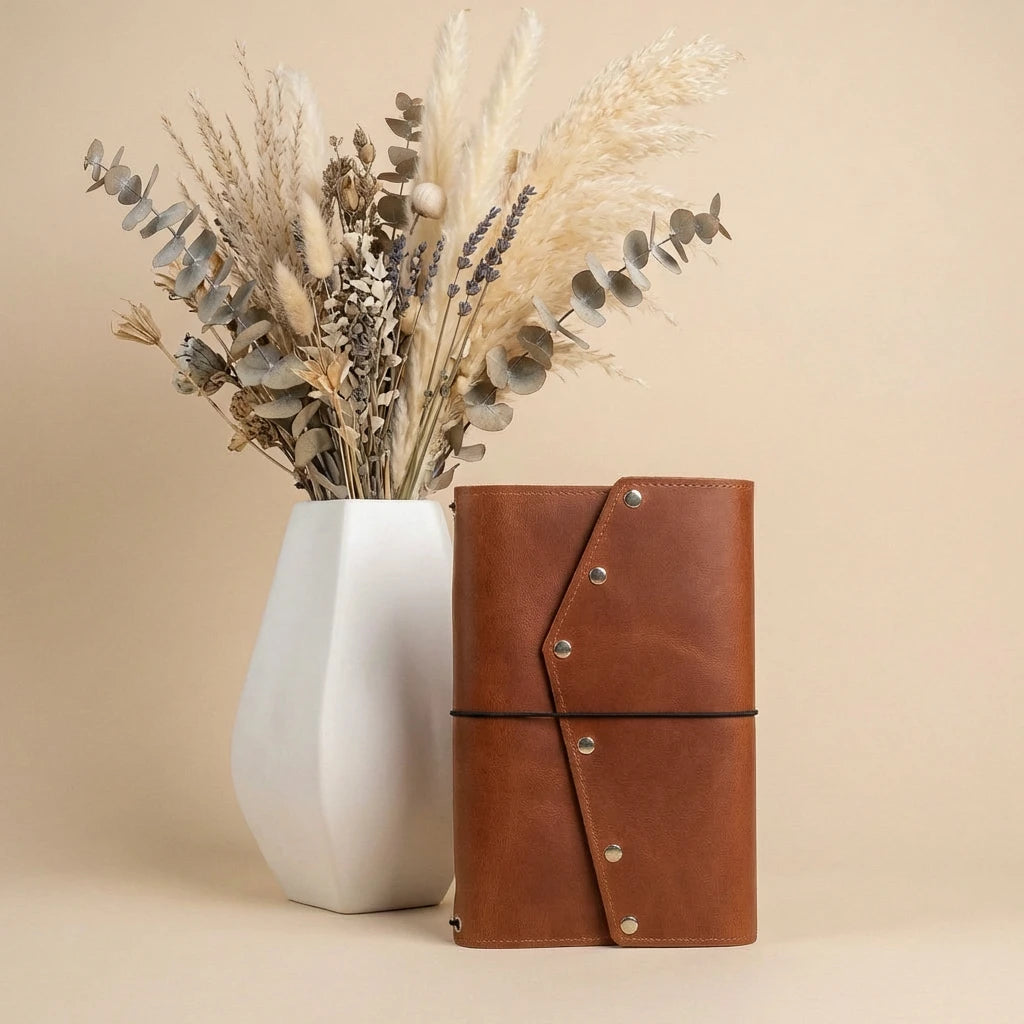 Brown leather notebook and white vase with dried plants on a beige background